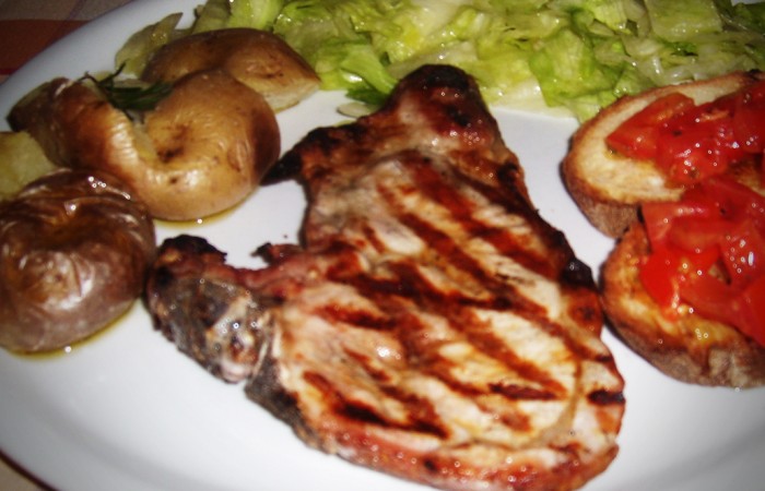 Costata di maiale, insalata, patate al forno e bruschette